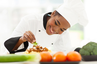 Cheerful Chef in white uniform garnishing a dish in a professional kitchen with fresh vegetables in the foreground.