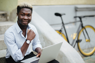 Young person sitting on steps using laptop with bicycle in background