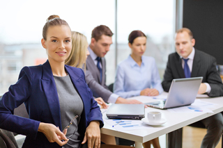 Businesswoman in blue blazer with colleagues working in background in an office setting.