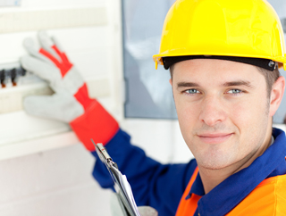 Male electrician in yellow hard hat and safety gloves working on a fuse box.