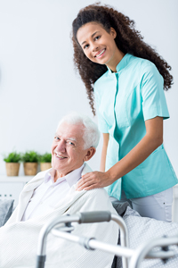 Young nurse with curly hair assisting an elderly patient in wheelchair in a healthcare setting.