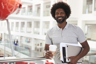 Man with afro holding a laptop and coffee cup.