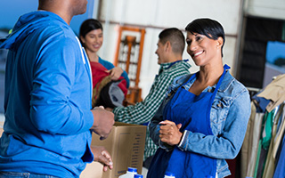 Group of volunteers sorting donations in a warehouse, woman smiling and interacting with a colleague.