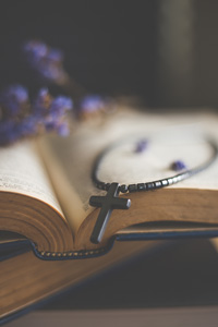 Silver cross necklace on an open Bible with blurred lavender flowers in the background