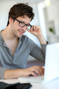 Young man with glasses and a gray shirt working on laptop.