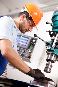 Industrial worker in blue uniform and orange safety helmet operating a machine in a factory setting.