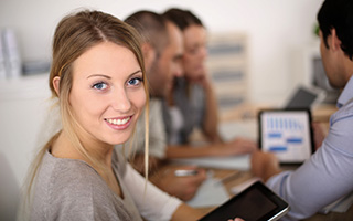 Woman with blonde hair at a meeting with colleagues using digital devices in an office.