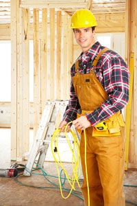 Construction worker in yellow hard hat and tool belt holding electrical wires in unfinished wooden building