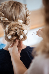 Elegant bridal hairstyle with braids and white floral accessories viewed from behind in a mirror reflection.