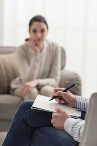 Woman in therapy session with psychologist taking notes in foreground.