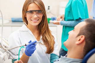 Dentist in safety glasses and gloves holding dental tools while talking to a patient in a dental clinic.