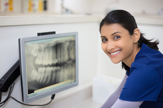 Dental assistant in blue scrubs looking at dental X-ray on a computer screen in a dental office.