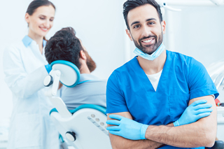 Dental hygienist wearing blue scrubs in dental clinic with female colleague and patient in background