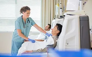 Nurse adjusting dialysis machine for patient in hospital room.