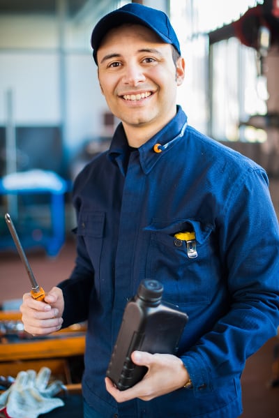 Diesel mechanic in blue uniform holding a screwdriver and an oil bottle in a workshop