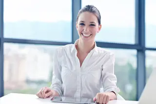 Businesswoman in white blouse sitting at desk in an office setting.