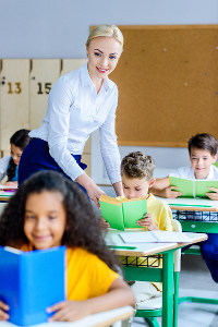 Teacher assisting diverse students in a classroom, students reading books at desks