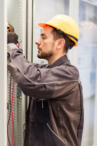 Electrician in a gray uniform and yellow hard hat working on wiring in an industrial setting