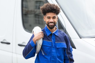 Technician with curly hair holding cables and standing in front of a white van