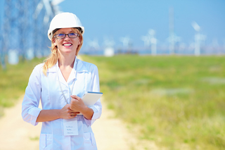 Engineer in hard hat and glasses holding a tablet with wind turbines in the background