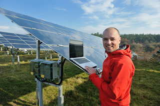 Man in red jacket using laptop to check solar panel efficiency in a field