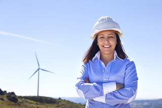 Engineer in hard hat standing in front of wind turbines on a clear day