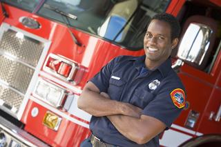 African American firefighter in front of a red fire truck.