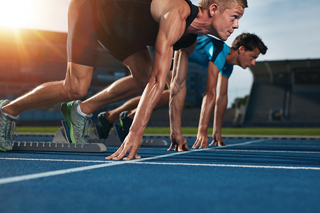 Two male athletes in starting positions on a track field at sunset, ready to sprint