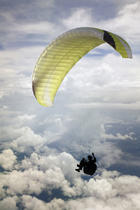 Paraglider soaring above clouds with a yellow and black canopy against a sky background