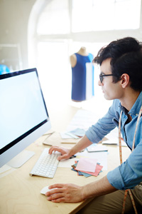 Fashion designer using computer in studio with fabric swatches