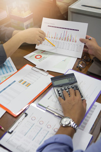 Two professionals analyzing financial data charts and using a calculator at an office desk.