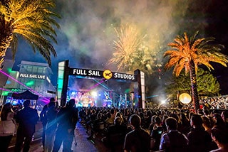 Crowd watching fireworks display at night outside Full Sail Studios during an event.