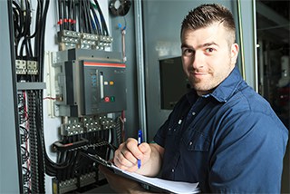 Electrician with clipboard conducting maintenance on an industrial electrical cabinet