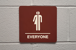 Gender-inclusive restroom sign with symbol and text reading EVERYONE on a brick wall.