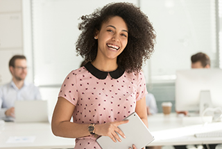 Happy young businesswoman holding a tablet in an office environment with colleagues in the background