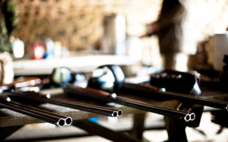 Guns on a table, background hint of a person working in a workshop.