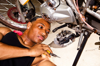 Young man repairing a motorcycle engine, lying on the floor in a garage, holding a wrench.