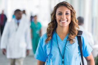 smiling health care professional in blue scrubs walking in a busy hospital hallway