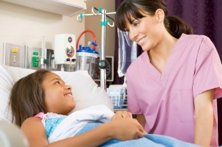female nurse in pink scrubs smiles at child patient in hospital bed