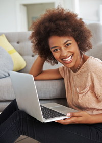 Happy young woman with curly hair using laptop on couch at home