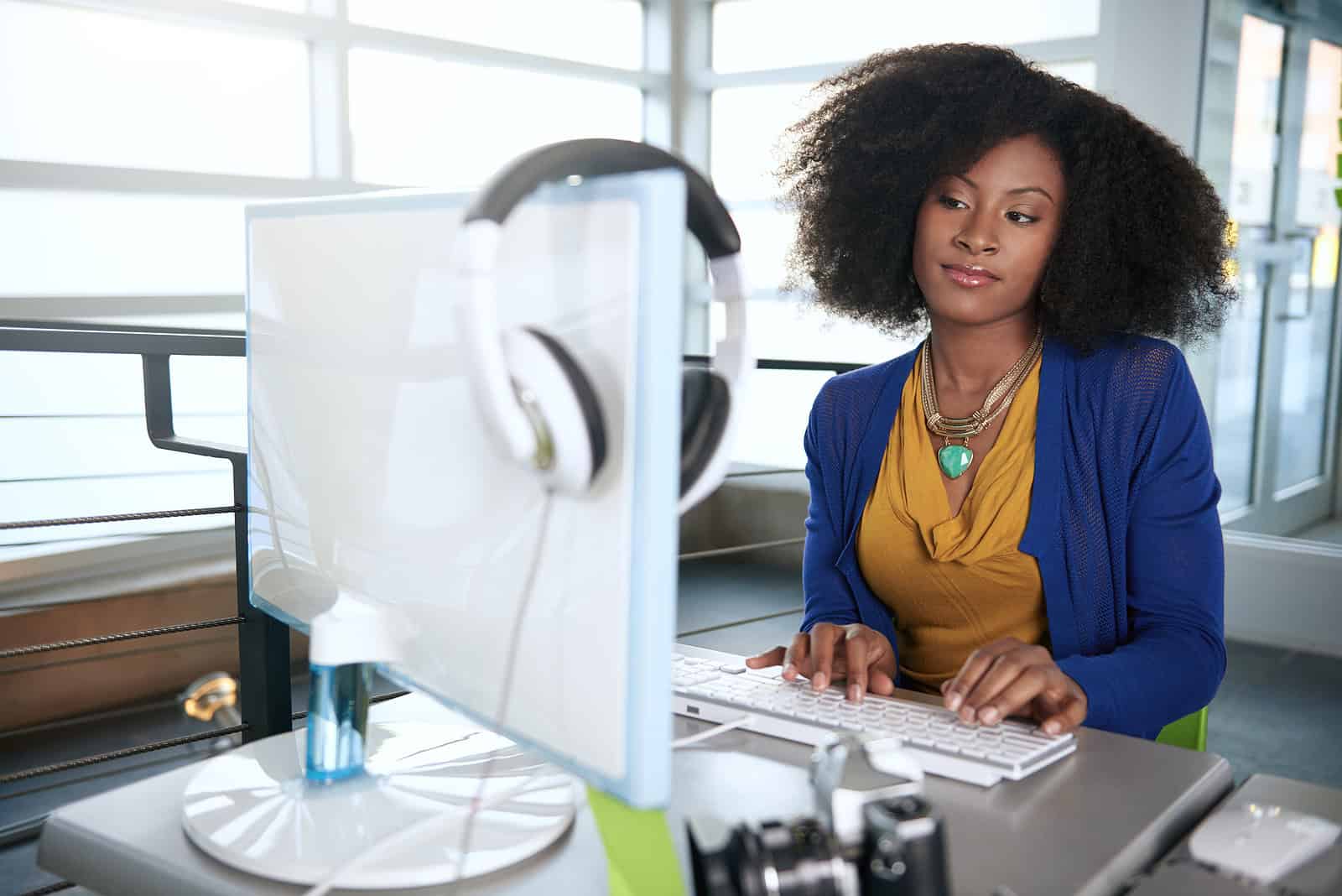 Professional African American woman working at a computer desk in an office setting with headphones