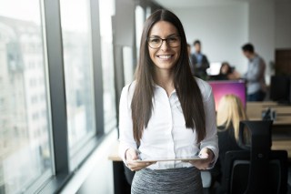 Happy, young female business professional standing by a window in an office