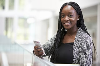 female professional in a yellow sweater and a scarf smiling and working on a laptop