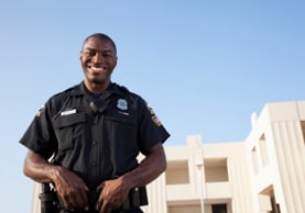African American police officer standing in uniform with a clear blue sky in the background.
