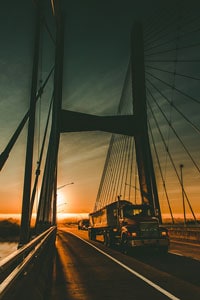 Truck driving on cable-stayed bridge at sunset with silhouette of suspension cables and vibrant sky