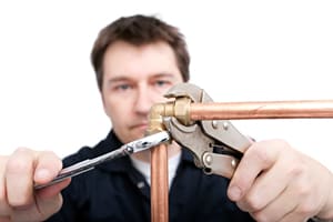 Plumber using wrench to tighten fitting on copper pipe, isolated on white background