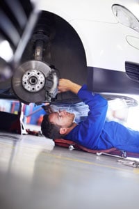 Mechanic in blue uniform working under a car on a creeper in a garage