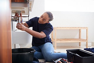 Woman repairing sink plumbing with tools in a home setting