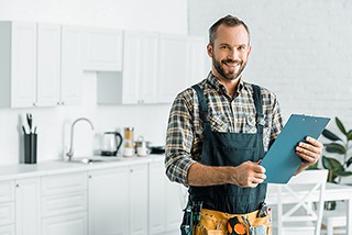 Male carpenter with beard holding clipboard in modern kitchen while wearing plaid shirt and tool belt