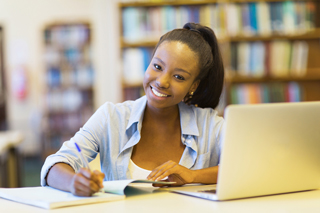 Young woman studying with laptop and notebook in library